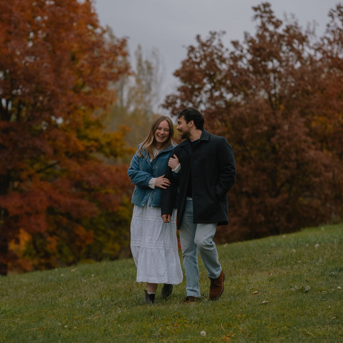 Two people walking together in a park with trees displaying autumn colors.